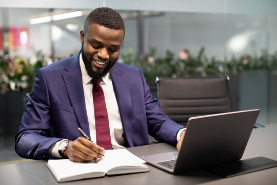 Happy african american businessman using laptop and taking notes