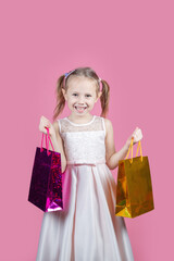 Cute little girl in a party dress on pink background holding colorful bags