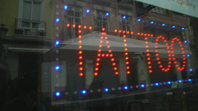 Cartel led con las palabras TATTO tras un escaparate donde se reflejan los edificios de enfrente