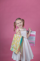 Cute little girl in a party dress on pink background holding colorful bags