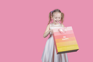 Fototapeta premium Adorable girl holding shopping bags against pink background with copy space.
