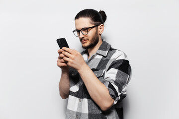 Studio photo of attractive young guy, in plaid shirt, holding smartphone.