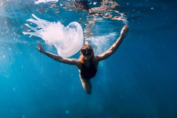 Woman underwater with jellyfish in blue ocean. Lady glides underwater in sea