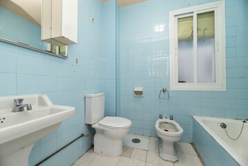 Toilet with blue square tiled walls, white wooden door and white toilets. white aluminum window and bathtub