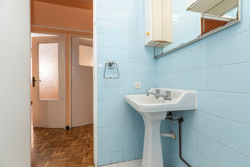 Toilet with blue square tiled walls, white wooden door and white toilets. Framed mirror with furniture