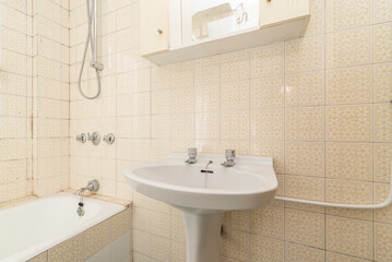 Vintage bathroom with kitsch yellow daisy tile, white porcelain tub and fixtures, and cabinet over sink