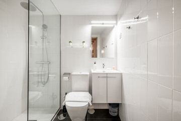 Bathroom with white wooden furniture, shower with glass partition and square mirror above the sink