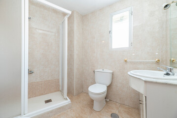 Fototapeta na wymiar Bathroom with white wooden cabinets, shower cabin with screen and small window in the wall