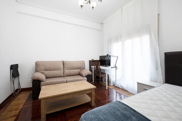 Room with bed and sofa bed, white study table, coffee table and varnished oak parquet floors