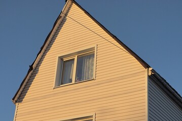 brown plastic attic of a private house with one window on the street against a blue sky