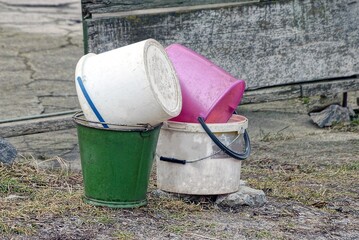 a pile of old colored plastic and metal buckets stand on the ground and grass on the street