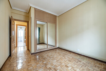 empty room with oak parquet, yellow painted walls and built-in wardrobe with sliding mirror doors and trunk with wooden doors