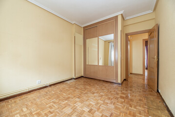 empty room with oak parquet, yellow painted walls and fitted wardrobe with sliding mirror doors and chest with wooden doors and French oak bedroom door