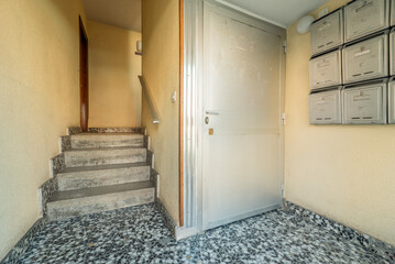 Entrance portal to a modest residential house with gardens, terrazzo floors, iron mailboxes and aluminum doors