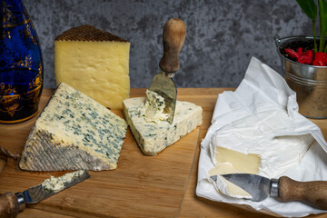 Still life with assorted cheeses, cured sheep, blue salted cow, brie and blue glass bottle with glasses
