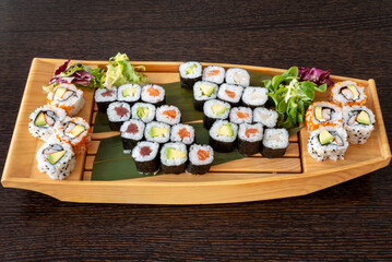 Sushi tray in the shape of a Japanese wooden boat with uramaki california roll, tuna maki, Norwegian salmon maki, ripe avocado maki and salmon and surimi uramaki