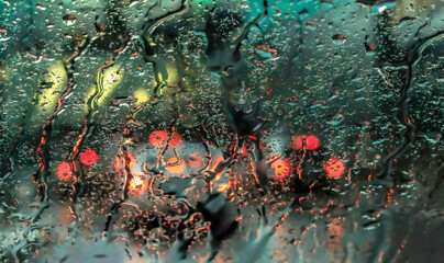 View looking through a car windshield  window wet with rain streaks, blurry car taillights, green toning