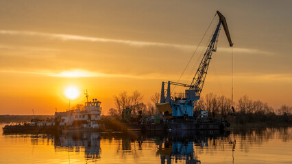 Obraz premium Vessel engaged in dredging at sunset time. Ship excavating material from a water environment.