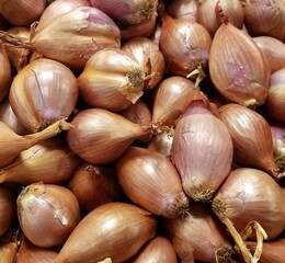 Close up view of a pile of multiple shallot onions displayed at a fresh food produce farmers market. Garden to store freshness. Raw ingredient for culinary dishes. Natural lighting. 