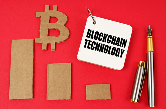 On a red surface lie the bitcoin symbol, a pen and a notepad with the inscription - Blockchain technology