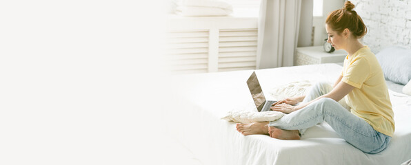 Beautiful young woman working remotely or studying at home at her laptop in her bedroom. Banner, copy space for text