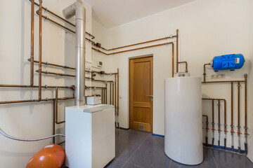 Boiler room of a country house with white tanks and a system of pipes for heating.