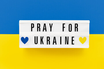 PRAY FOR UKRAINE written in a lightbox on Ukrainian flag colors background