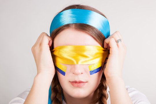 Young woman with painted ukrainian flag on her cheeks takes off her blindfold isolated on white background. National colors and symbols of Ukraine.