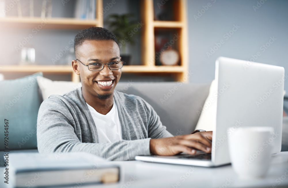 Wall mural I stay connected so I dont miss out on anything. Portrait of a happy young man using a laptop while relaxing at home.