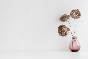 White desk with minimal vase with a decorative dried branches, flower against white wall...