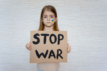 Upset toddler girl protesting war conflict raises banner with inscription massage text Stop War....