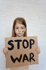 Upset toddler girl protesting war conflict raises banner with inscription massage text Stop War....
