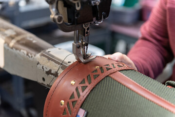 Skilled hands of factory worker guiding the embroidery sewing thread around the border of the leather bag in production