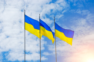 Banner with three Ukrainian flags on a background of blue sky and rising sun . High quality photo