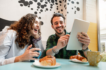 young couple smiling looking something at tablet. People sitting at table in a cafe having...