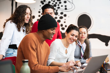 Mixed group of young smiling people looking at computer laptop with positive actitude. Students or co-workers discussing.