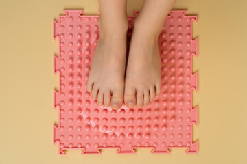 children's feet on a pink orthopedic mat on a beige background, treatment and prevention of flat feet, hallux valgus, a place for text