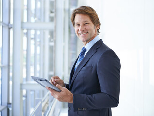 Fototapeta premium Its great being able to tweet on the job. Shot of a mature businessman standing in an office corridor using a digital tablet.