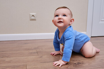 Baby toddler is near the electrical outlet on the home wall. Danger and protection of child fingers...