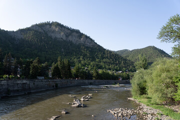 a large river with little water where there are stones and green trees along the shore, and some pieces of concrete can be seen in the middle