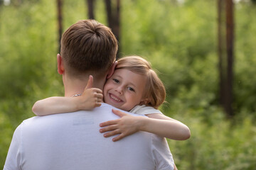 Dad and daughter walk in the forest in summer, the girl hugs dad by the neck
