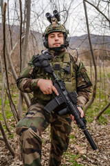 Fototapeta premium one man front view portrait of soldier in camouflage uniform armed with rifle ready to go on a mission in war zone standing outdoor in nature looking to the camera dogs of war mercenaries or volunteer