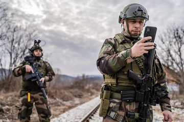 Fotobehang Two soldiers dogs of war mercenaries men in uniform armed service rifles standing while securing the railroad in combat zone in war soldier use mobile phone while patrolling area during mission © Miljan Živković