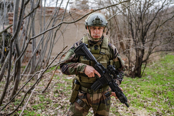 one man front view portrait of soldier in camouflage uniform armed with rifle ready to go on a mission in war zone standing outdoor in nature looking to the camera dogs of war mercenaries or volunteer