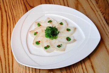 fish carpaccio garnished with coriander leaves and tomato chunks on wooden table