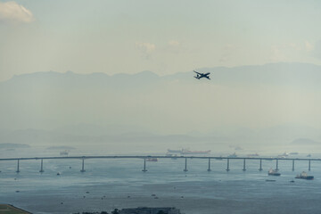 Airplane taking off from the airport runway in Rio de Janeiro, Brazil. Rio Niterói Bridge, mountains and ships in the background. Dawn with a little fog