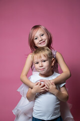 Caucasian brother and sister ,hugging on camera on pink background studio shot.