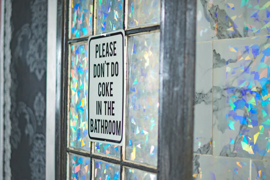 No coke in the bathroom sign, on a stylish bathroom door in natural morning light, in white bathroom tile glass reflection, party lifestyle, drug culture theme, funny sign.
