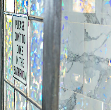 No coke in the bathroom sign, on a stylish bathroom door in natural morning light, in white bathroom tile glass reflection, party lifestyle, drug culture theme, funny sign.