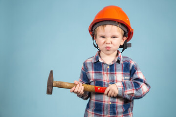 Adorable caucasian child in orange safety helmet,holdings hammer at hands.